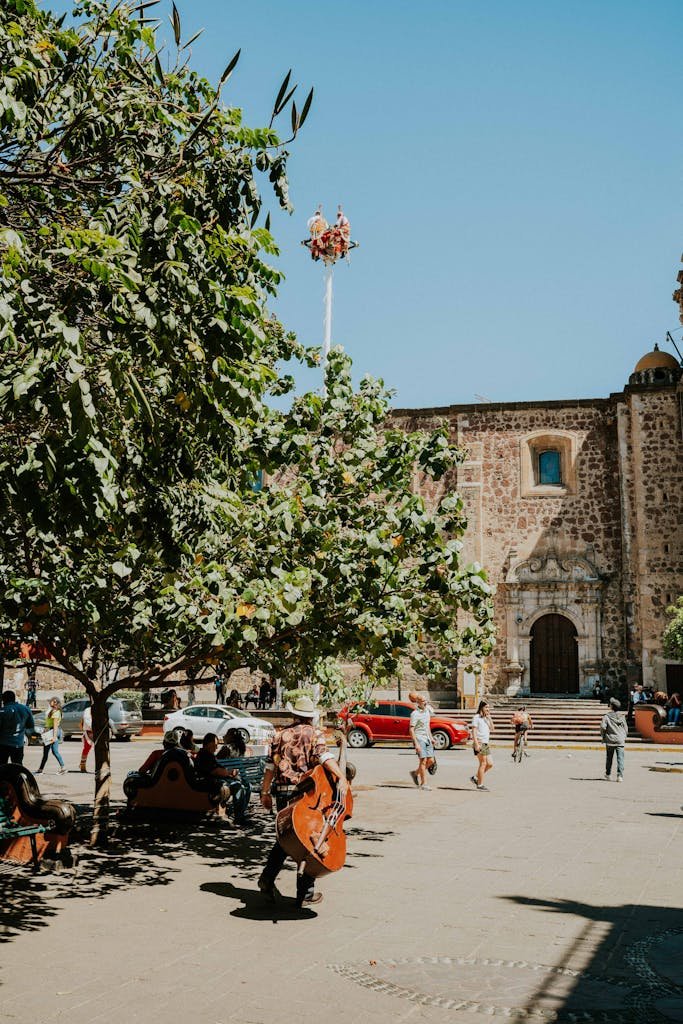 A vibrant plaza scene with a cellist performing under the sun in Guadalajara, Mexico.